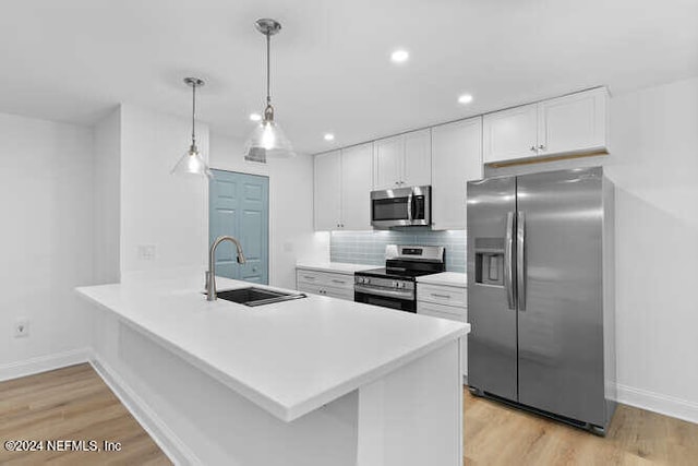 kitchen with kitchen peninsula, stainless steel appliances, sink, white cabinetry, and hanging light fixtures