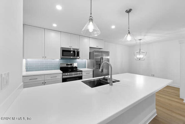 kitchen with stainless steel appliances, sink, decorative light fixtures, white cabinets, and light hardwood / wood-style floors