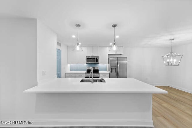 kitchen featuring appliances with stainless steel finishes, sink, light hardwood / wood-style flooring, white cabinetry, and hanging light fixtures