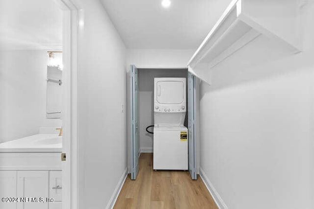 hallway with stacked washer / dryer, sink, and light hardwood / wood-style floors