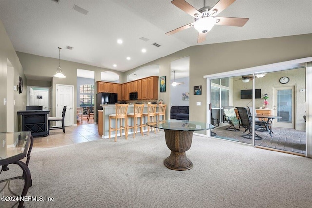 interior space with vaulted ceiling, decorative light fixtures, a kitchen bar, light carpet, and black appliances