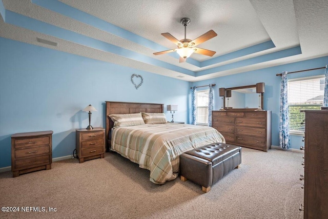 bedroom featuring light carpet, a textured ceiling, a raised ceiling, and ceiling fan