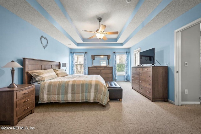 bedroom featuring a textured ceiling, light colored carpet, ceiling fan, and a tray ceiling