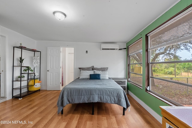 bedroom with a wall mounted AC and light hardwood / wood-style floors