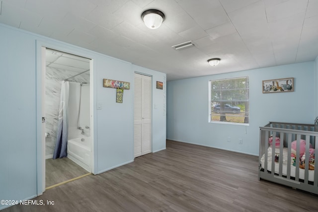 bedroom featuring hardwood / wood-style flooring, a nursery area, connected bathroom, and a closet