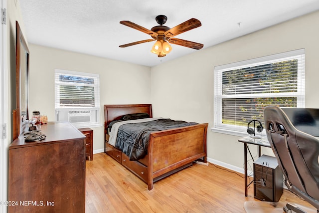 bedroom featuring ceiling fan, cooling unit, light wood-type flooring, and multiple windows