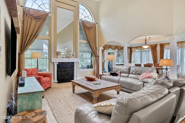 living room featuring a towering ceiling, decorative columns, ornamental molding, light tile patterned floors, and a tiled fireplace