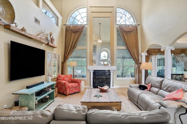 living room featuring a tiled fireplace, ornate columns, ceiling fan, and a high ceiling