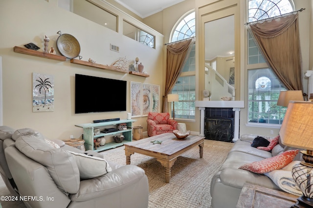 living room featuring a tiled fireplace, crown molding, a healthy amount of sunlight, and a high ceiling