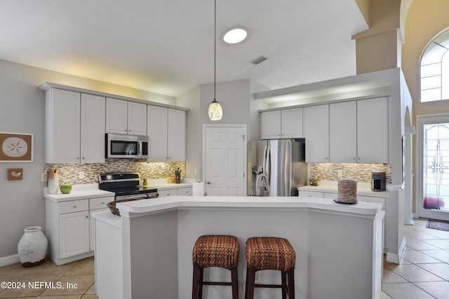 kitchen featuring appliances with stainless steel finishes, backsplash, a kitchen island with sink, light tile patterned floors, and pendant lighting