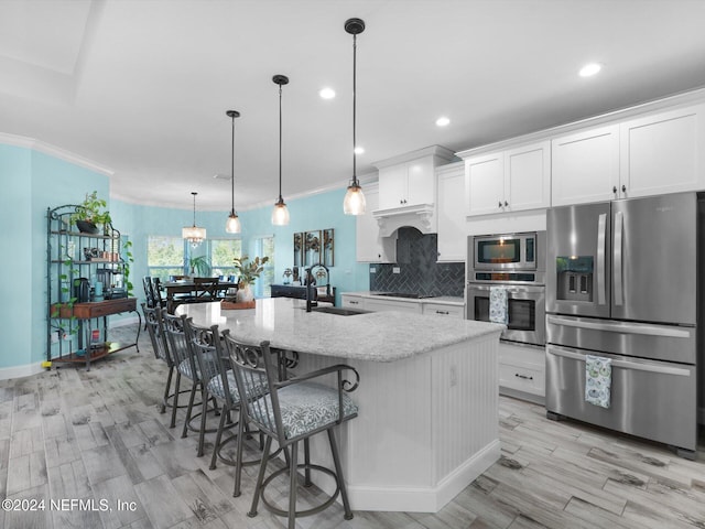 kitchen with hanging light fixtures, ornamental molding, an island with sink, appliances with stainless steel finishes, and white cabinetry