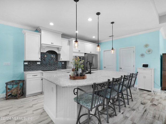 kitchen with white cabinets, a large island with sink, pendant lighting, and a breakfast bar area