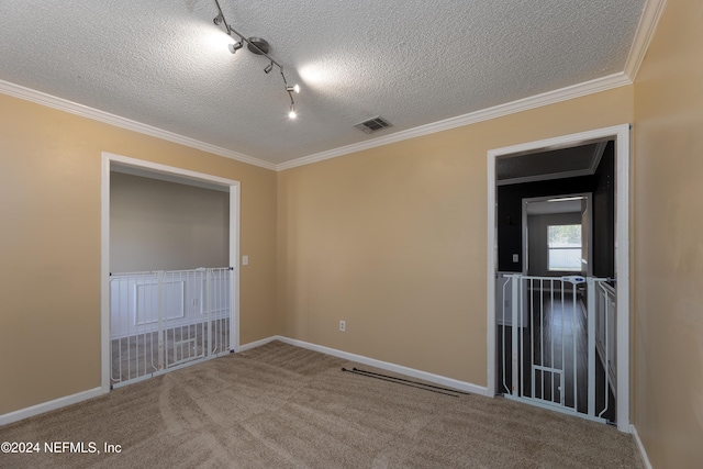 empty room featuring a textured ceiling, carpet floors, rail lighting, and ornamental molding