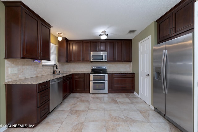 kitchen with sink, stainless steel appliances, tasteful backsplash, light stone counters, and a textured ceiling