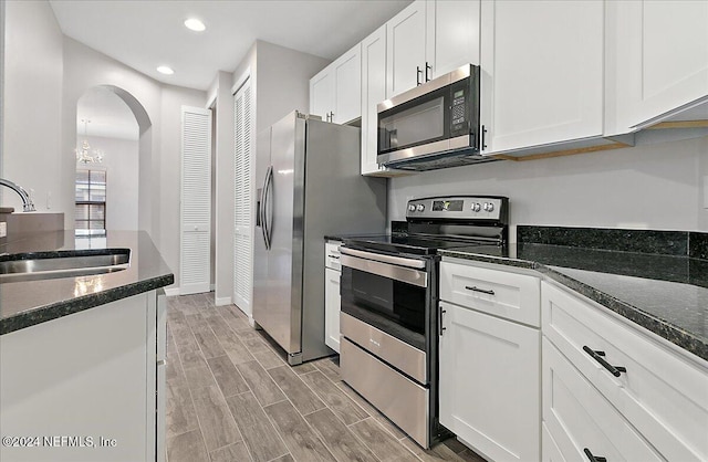 kitchen featuring appliances with stainless steel finishes, sink, dark stone countertops, light hardwood / wood-style floors, and white cabinetry