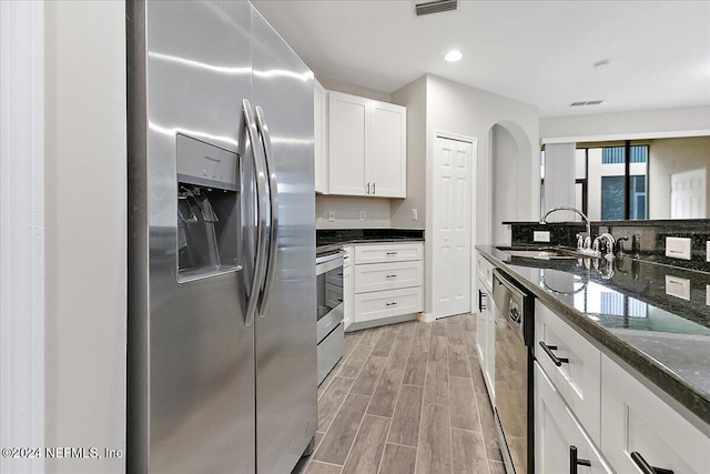 kitchen with dark stone counters, sink, light hardwood / wood-style floors, white cabinetry, and stainless steel appliances