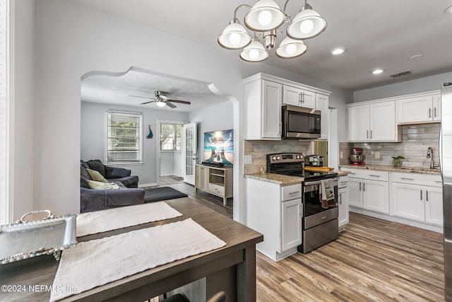 kitchen with light hardwood / wood-style flooring, white cabinets, hanging light fixtures, and appliances with stainless steel finishes