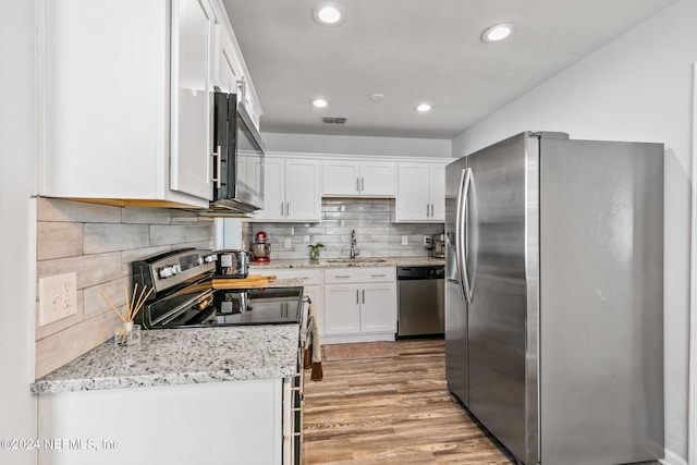 kitchen featuring white cabinets, sink, light stone countertops, appliances with stainless steel finishes, and light hardwood / wood-style floors