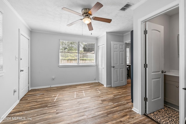 unfurnished bedroom featuring hardwood / wood-style floors, a textured ceiling, ceiling fan, and crown molding