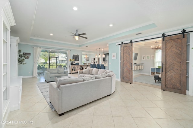 living room with a raised ceiling, a barn door, light tile patterned floors, ceiling fan with notable chandelier, and ornamental molding