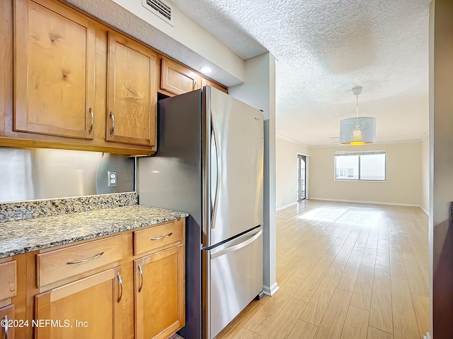 kitchen with stainless steel fridge, light wood-type flooring, light stone counters, and ornamental molding