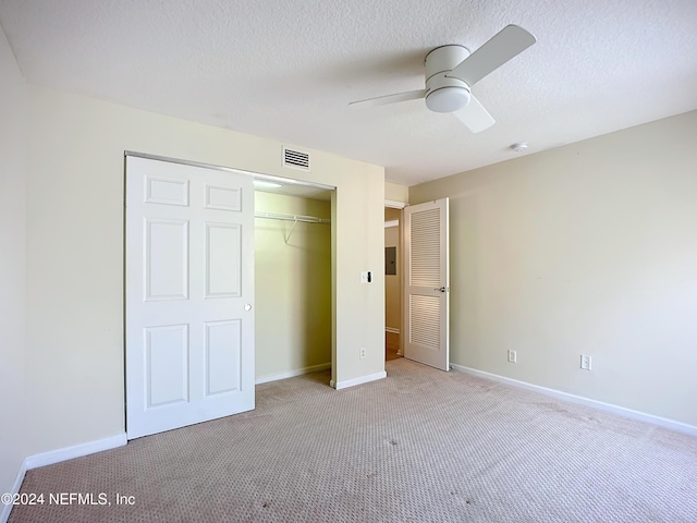 unfurnished bedroom featuring a textured ceiling, a closet, light colored carpet, and ceiling fan