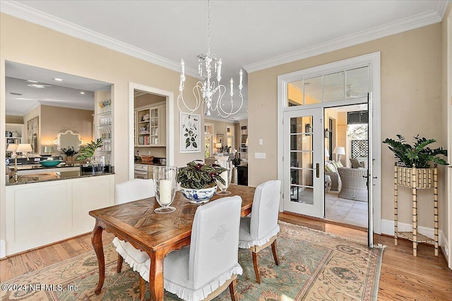 dining room featuring light wood-style flooring, french doors, crown molding, and an inviting chandelier