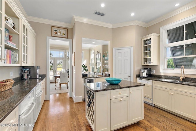 kitchen featuring visible vents, light wood-style flooring, a sink, white dishwasher, and crown molding