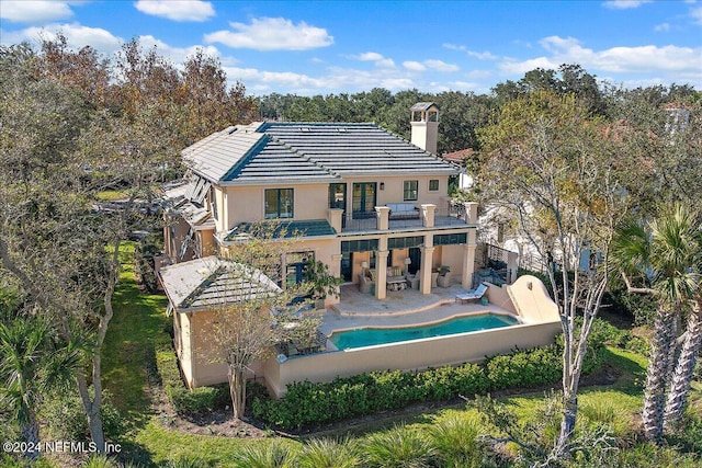 back of property featuring a tile roof, stucco siding, a chimney, a balcony, and a patio area