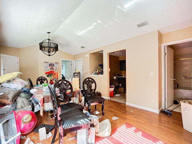 living room with a notable chandelier, vaulted ceiling, a textured ceiling, and light hardwood / wood-style flooring