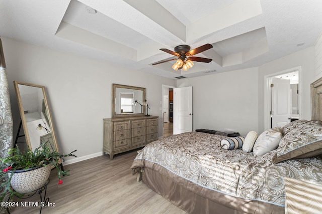 bedroom with a raised ceiling, ceiling fan, light hardwood / wood-style floors, and a textured ceiling