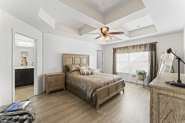 bedroom with ceiling fan, light hardwood / wood-style floors, a textured ceiling, and connected bathroom