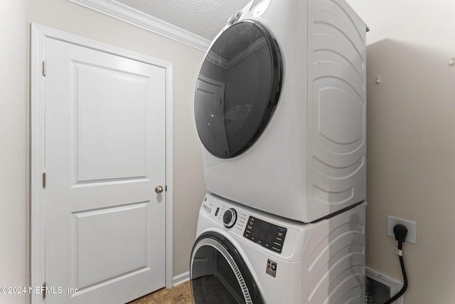 clothes washing area with ornamental molding, a textured ceiling, and stacked washer and clothes dryer