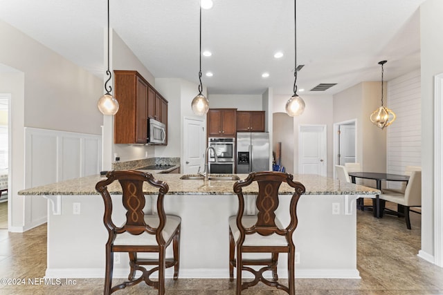 kitchen with light stone counters, a breakfast bar, hanging light fixtures, and appliances with stainless steel finishes