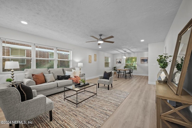 living room with ceiling fan, light wood-type flooring, and a textured ceiling