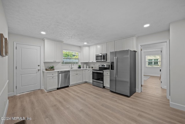 kitchen with white cabinets, sink, light hardwood / wood-style flooring, a textured ceiling, and appliances with stainless steel finishes