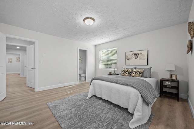 bedroom with ensuite bath, wood-type flooring, and a textured ceiling