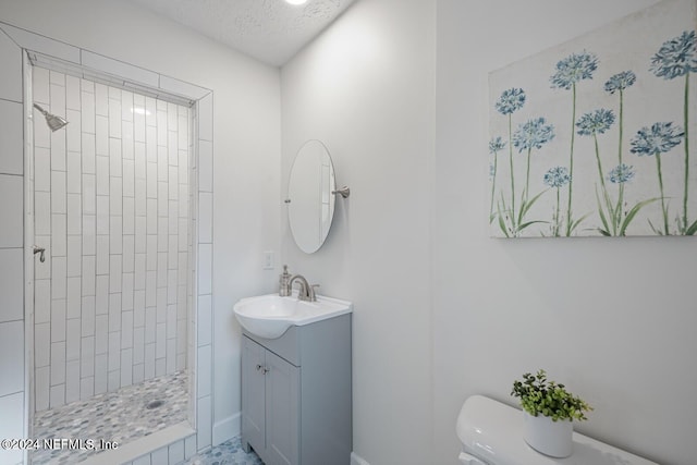 bathroom with tiled shower, vanity, a textured ceiling, and toilet