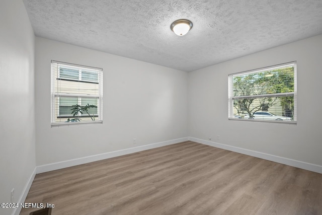 spare room featuring a textured ceiling, light hardwood / wood-style flooring, and a wealth of natural light