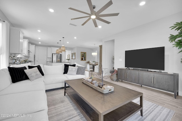 living room with ceiling fan with notable chandelier and light hardwood / wood-style floors