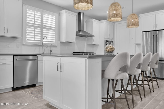 kitchen with white cabinetry, hanging light fixtures, wall chimney range hood, and appliances with stainless steel finishes