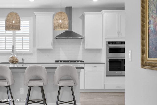 kitchen featuring white cabinetry, wall chimney range hood, and stainless steel appliances