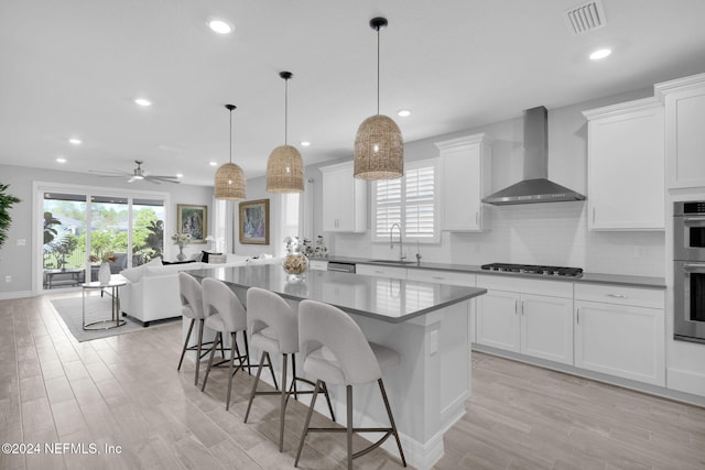 kitchen with pendant lighting, wall chimney range hood, light hardwood / wood-style flooring, ceiling fan, and stainless steel appliances