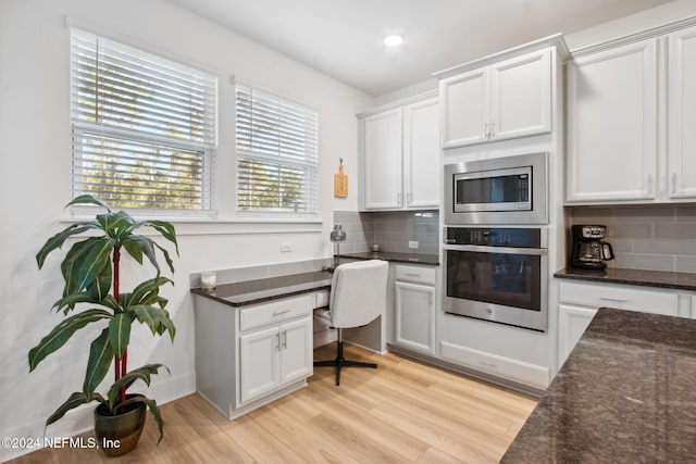 kitchen with backsplash, light hardwood / wood-style flooring, dark stone countertops, white cabinetry, and stainless steel appliances