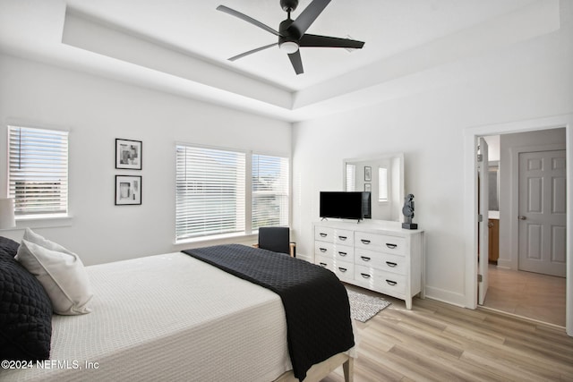 bedroom with light wood-type flooring, a raised ceiling, and ceiling fan