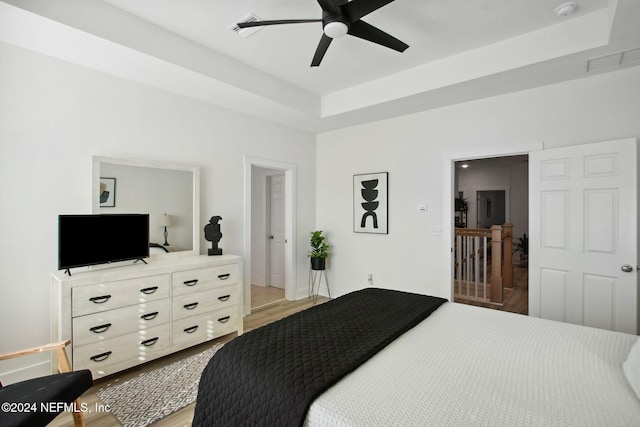 bedroom with ceiling fan, a raised ceiling, and wood-type flooring