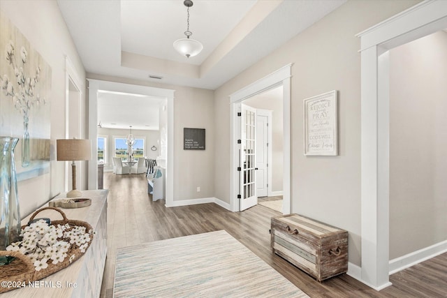 corridor with a tray ceiling, french doors, and wood-type flooring