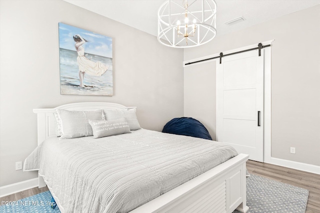 bedroom featuring a barn door, dark hardwood / wood-style flooring, and an inviting chandelier