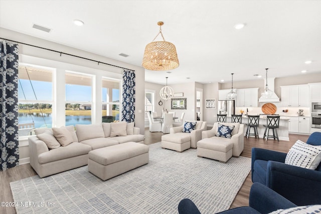 living room featuring an inviting chandelier, a water view, and light hardwood / wood-style flooring