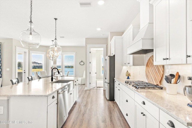 kitchen with decorative backsplash, custom exhaust hood, stainless steel appliances, a kitchen island with sink, and white cabinetry